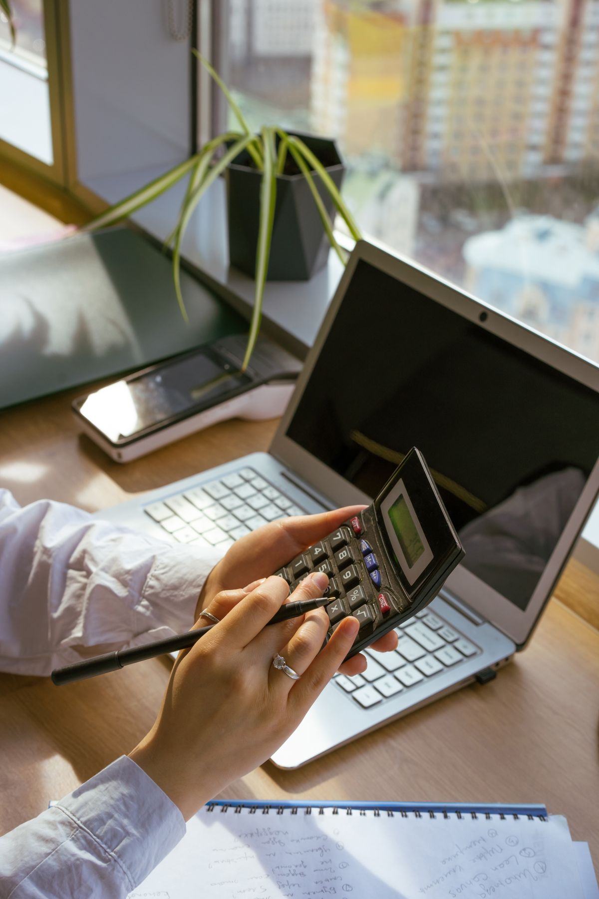 Person reviewing paperwork with a calculator and laptop